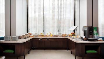 Un área de cocina moderna con cafetera, mesas de buffet y vistas amplias a través de grandes ventanales.