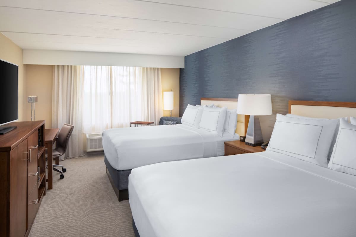 Une chambre d’hôtel avec deux lits, un bureau, une télévision et une fenêtre avec des rideaux.