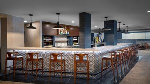 Un espace bar doté d’un long comptoir, de nombreux tabourets et de luminaires suspendus.