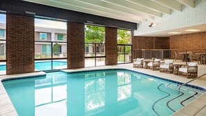 Une piscine intérieure avec des parois en verre transparent, un mur en briques et un espace détente avec des fauteuils en osier.