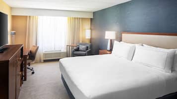 Ein Hotelzimmer mit einem großen Bett, einem Schreibtisch, einem Stuhl, einer Lampe und einem Fenster mit Vorhängen.