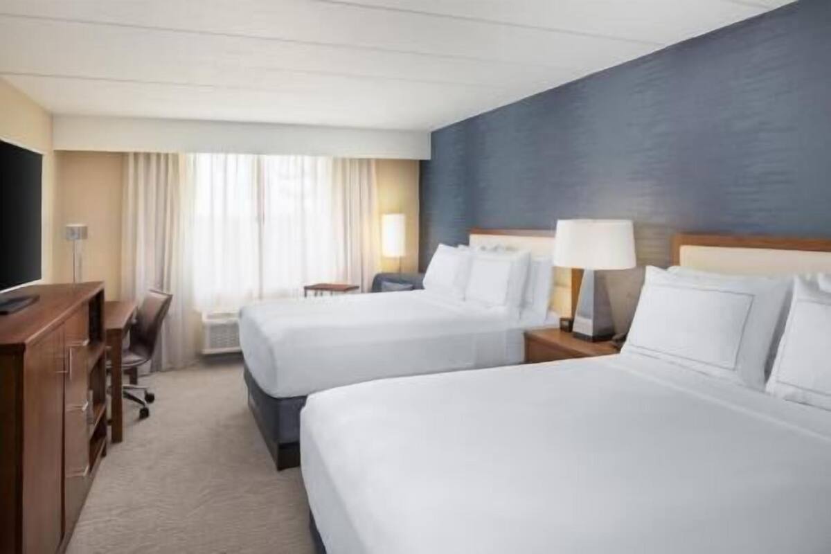 A hotel room with two beds, a desk, a chair, and a television.