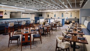 Un restaurant moderne doté de plusieurs espaces de restauration, notamment des banquettes et des tables, et d’un plafond haut avec des poutres apparentes.
