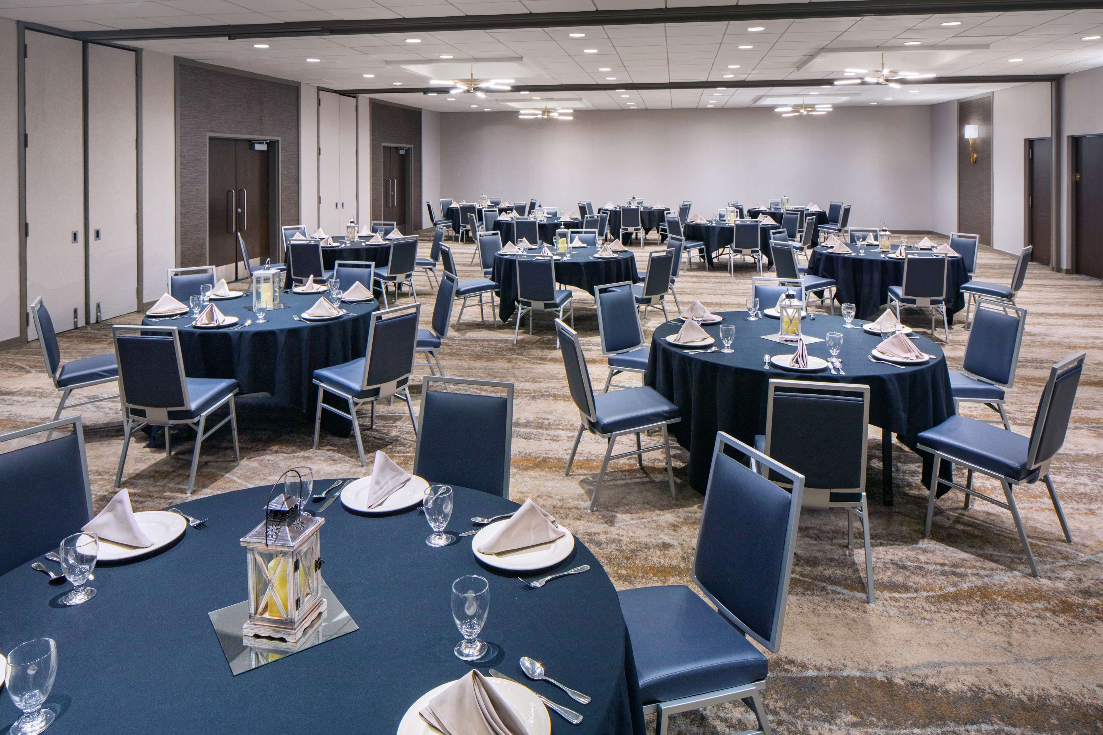 A conference room with multiple round tables, each set with chairs, plates, cutlery, and glassware.