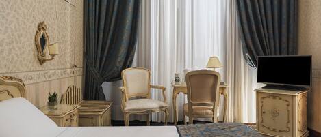 A hotel room with a bed, two chairs, a desk, a television, and curtains.