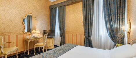 A hotel room with a large bed, a desk with a lamp, a chair, a television, and a mirror.