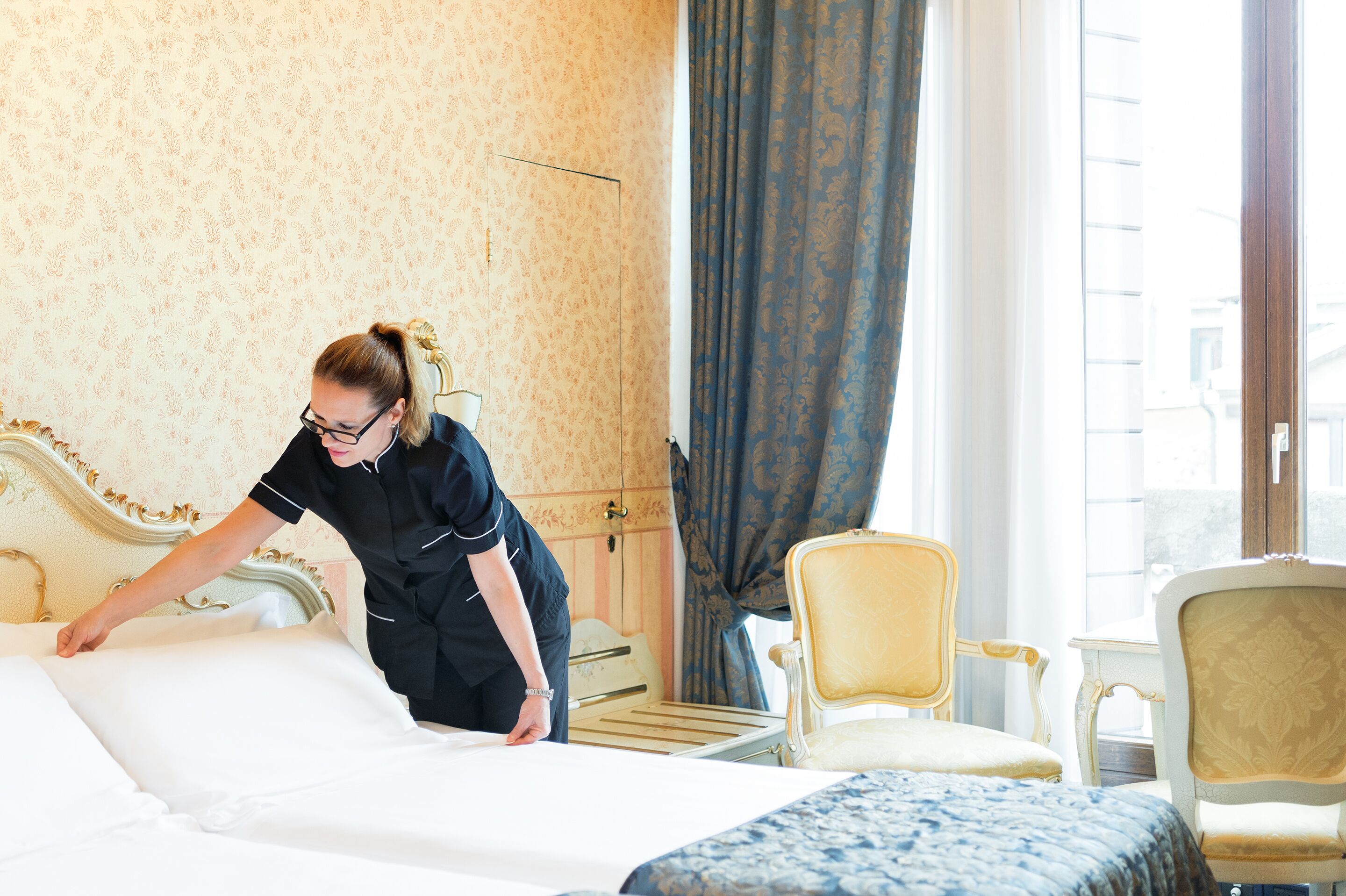 Una habitación de hotel con una cama, una silla y un ventanal con cortinas.