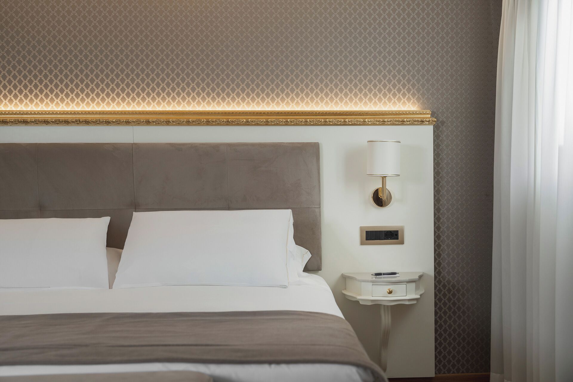 Habitación de hotel con una cama grande, una mesita de noche, una lámpara de pared y un papel tapiz estampado.