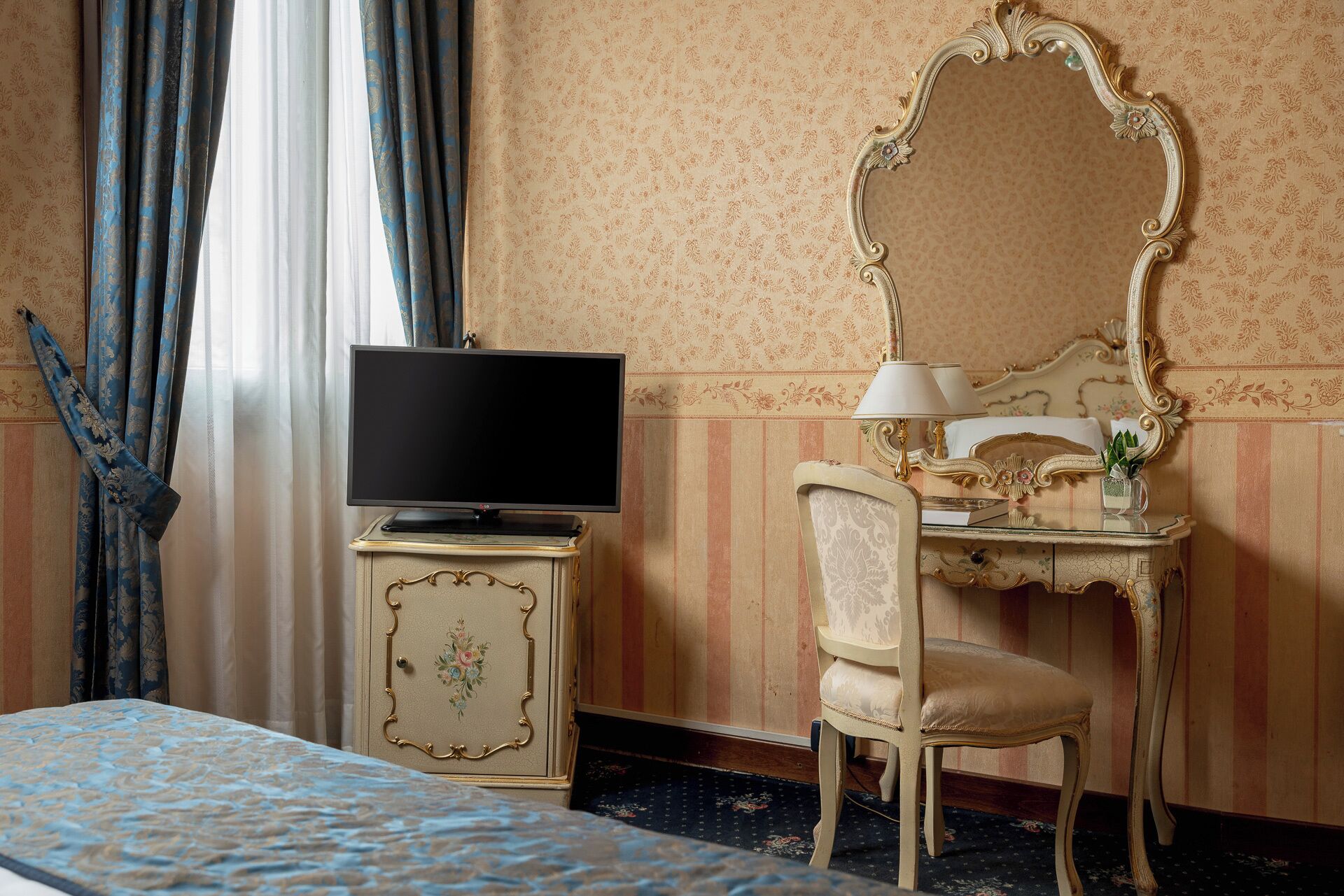 A hotel room with a bed, a television on a cabinet, a desk with a lamp, and a mirror.