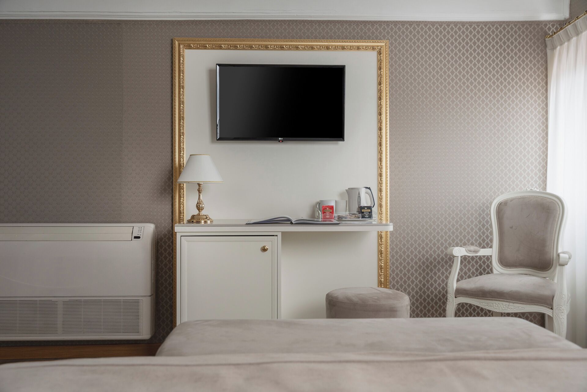 A hotel room with a bed, a desk with a lamp, a chair, a television, and a radiator.