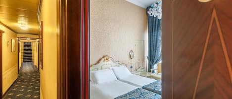 A hotel room with a double bed, a bedside table, a lamp, and a number sign.