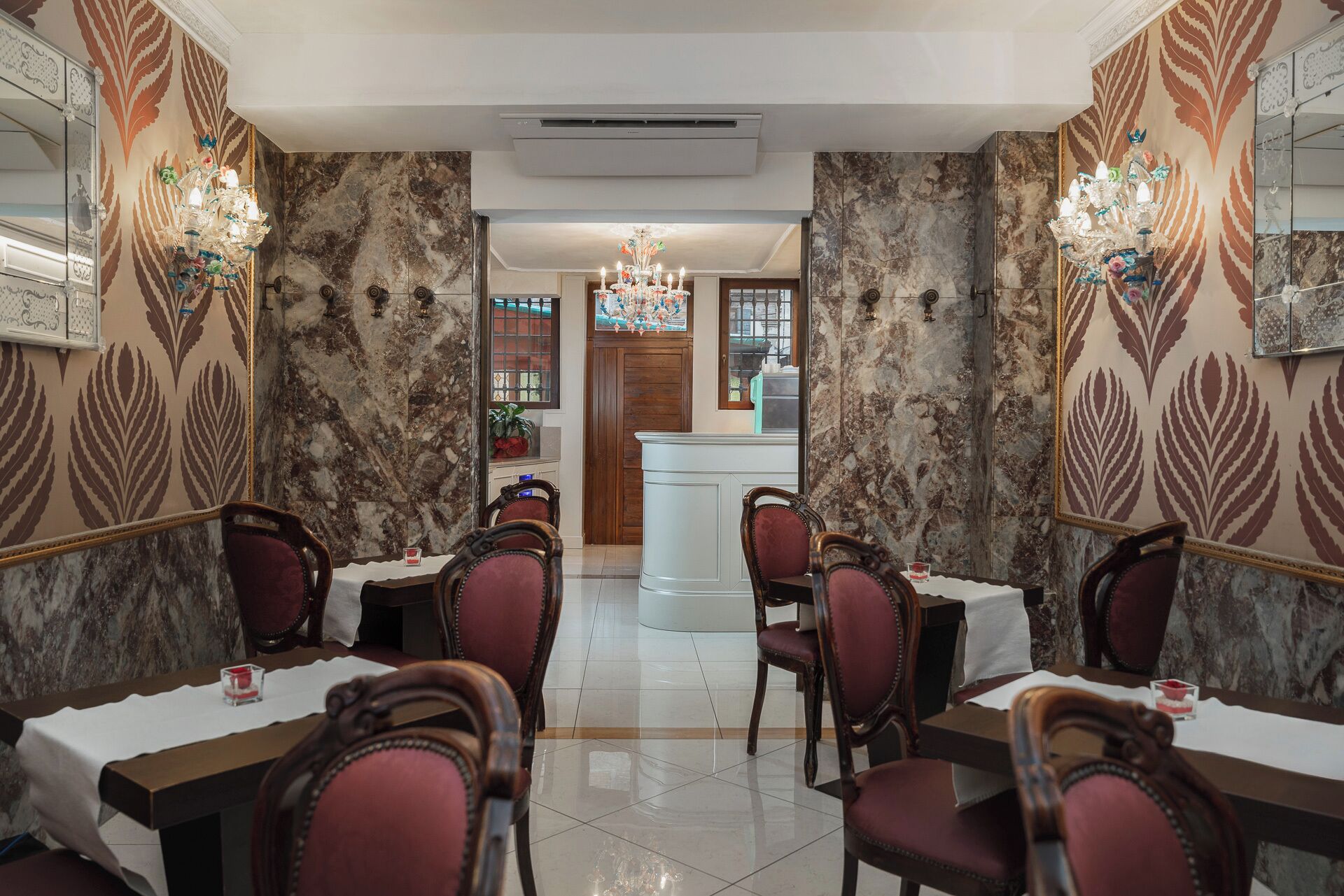A dining area with marble walls, chandeliers, and classic wooden chairs.