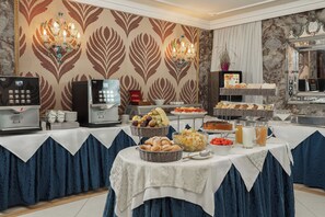 A buffet setup with a coffee machine, fruit, pastries, and beverages. - Hotel Montecarlo (Venice)