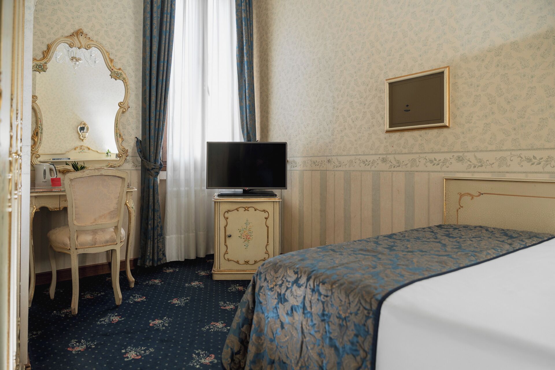 Una camera d'albergo con un letto, una scrivania con una sedia, una televisione e uno specchio.