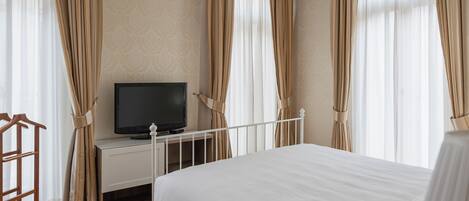 Una habitación de hotel con una cama, un televisor sobre un soporte blanco y cortinas.