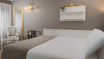 Habitación de hotel con cama, una silla, mesita de noche y estante de pared con un florero.