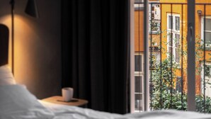 Une chambre à coucher avec un lit, une table de chevet avec une lampe et une fenêtre donnant sur un immeuble.