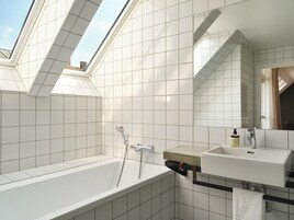 Un baño moderno con tragaluz, bañera, lavamanos y espejo.