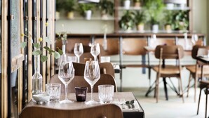 L’intérieur d’un restaurant est agrémenté de tables et de chaises en bois, ainsi que de diverses plantes en pot disposées sur des étagères.
