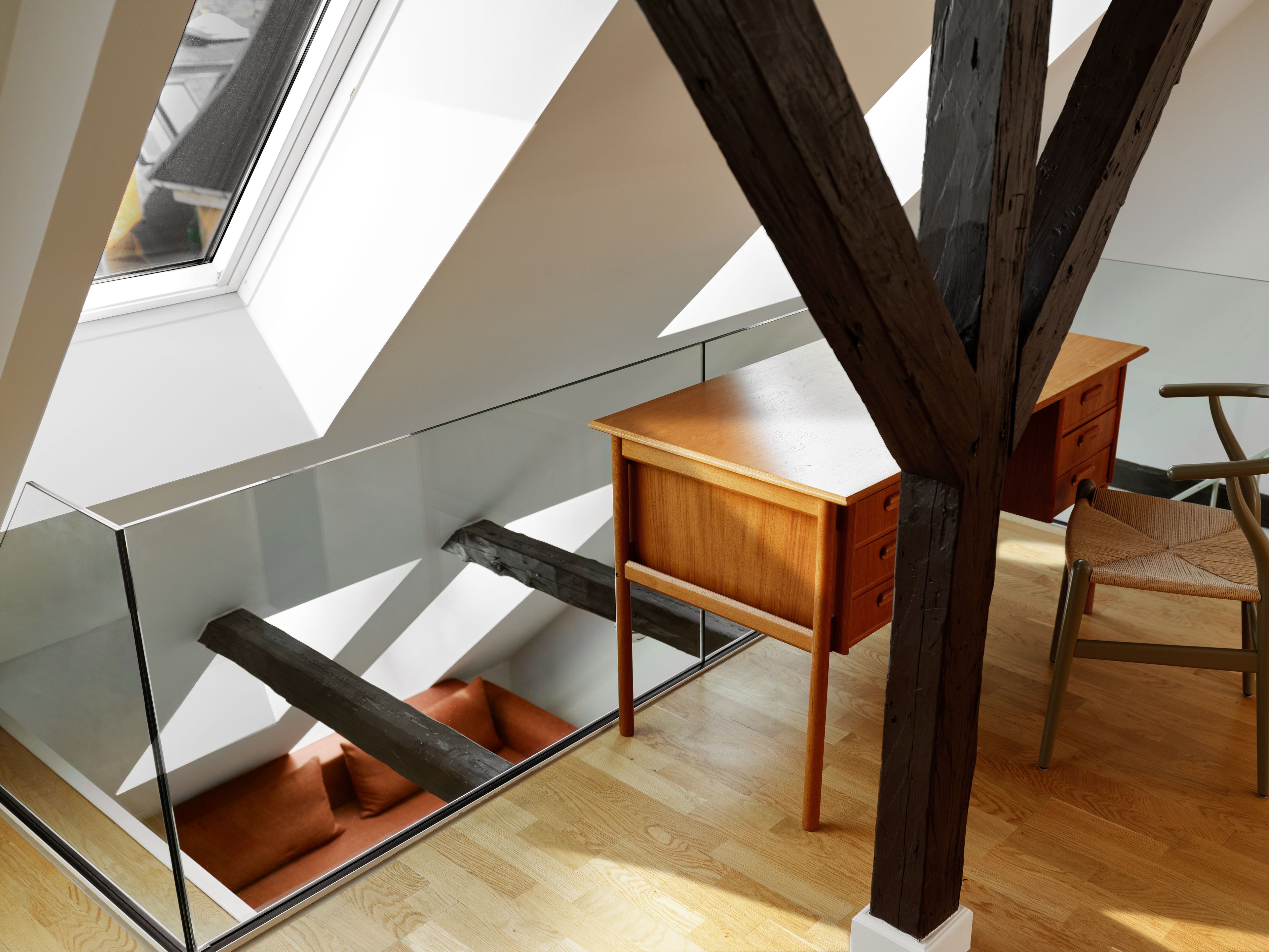 A modern loft bedroom with a sloped ceiling, a glass desk, a wooden chair, and a built-in bench.