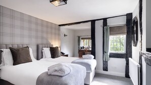 Habitació d'hotel amb dos llits, un finestral gran amb cortines, un radiador i una làmpada fixada a la paret.