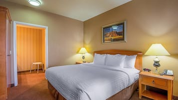 Habitació d'hotel amb un llit, dues làmpades de nit, una tauleta de nit, un quadre al mur i una porta que dona a una altra habitació.