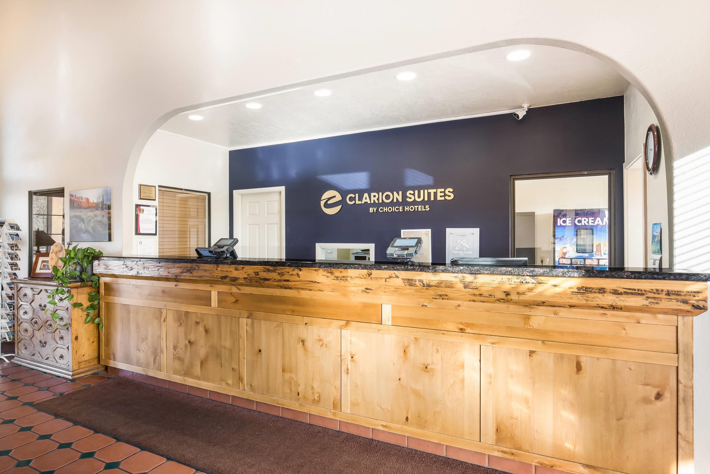 A reception desk with a wooden counter, a sign reading 'Clarion Suites by Choice Hotels,' and a reflection of an ice cream machine in the mirror.