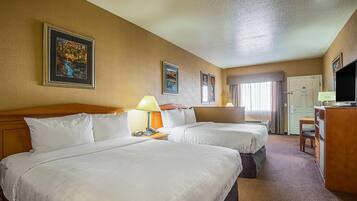 A hotel room with two beds, a desk, a TV, and framed pictures on the wall.