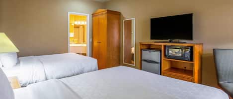 Quarto de hotel com duas camas, televisão, frigorífico e guarda-roupa de madeira.