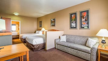 A hotel room with a bed, a sofa, a desk, a lamp, and two framed pictures on the wall.