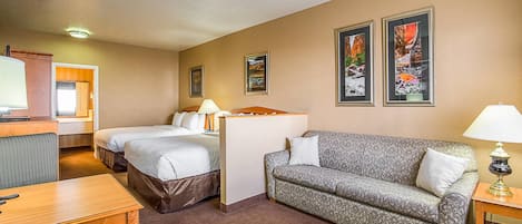A hotel room with a bed, a sofa, a desk, a lamp, and two framed pictures on the wall.
