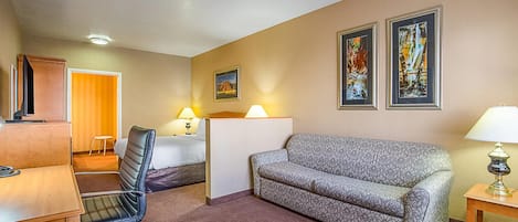 Habitación de hotel con escritorio, silla, sofá, dos lámparas, cama y dos cuadros en la pared.