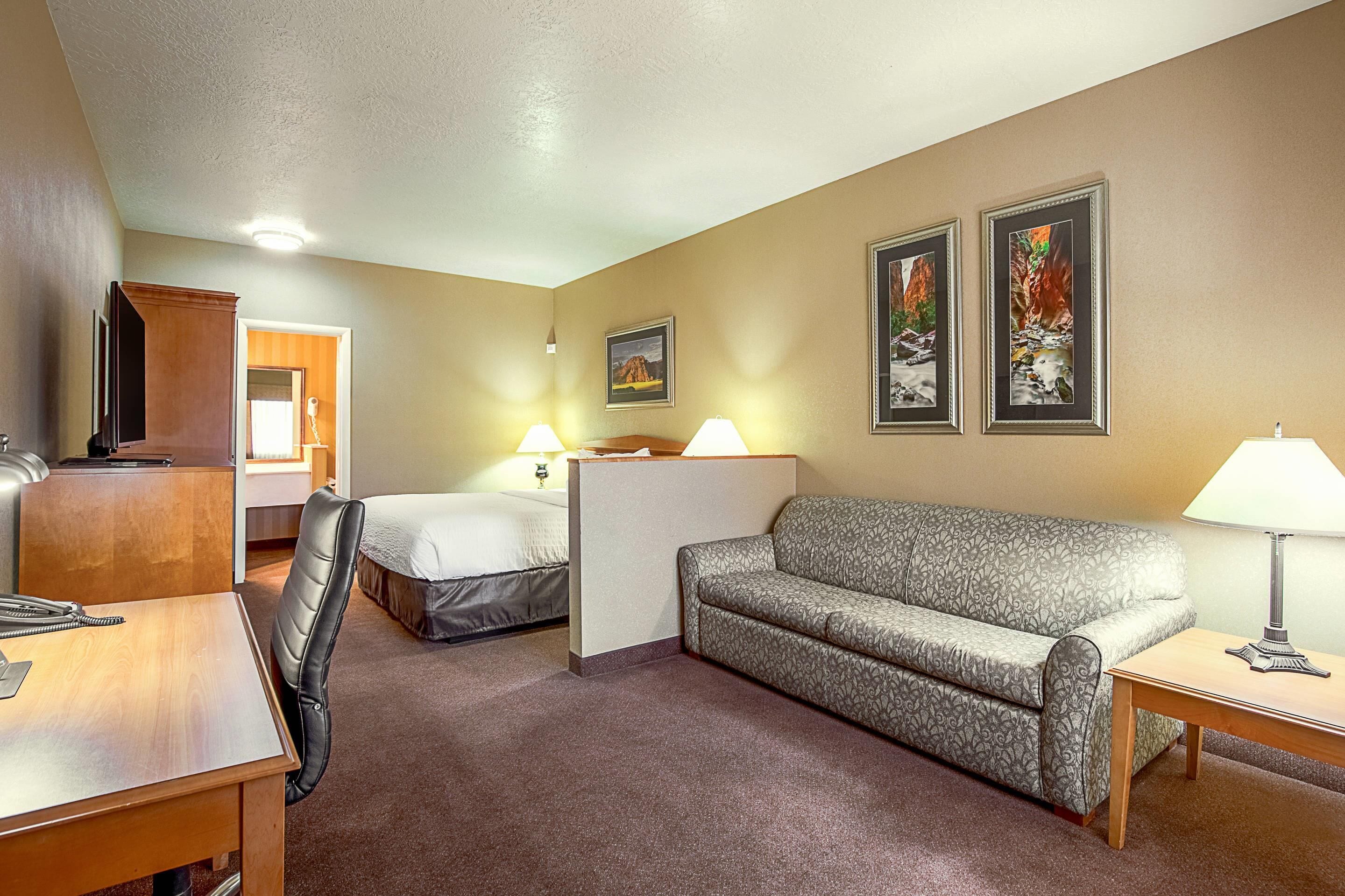 A hotel room with a bed, a sofa, a desk with a telephone, and two lamps.