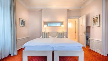 Una habitación de hotel con una cama grande, dos mesitas de noche, un ventanal con cortinas y una puerta que da a otra estancia.