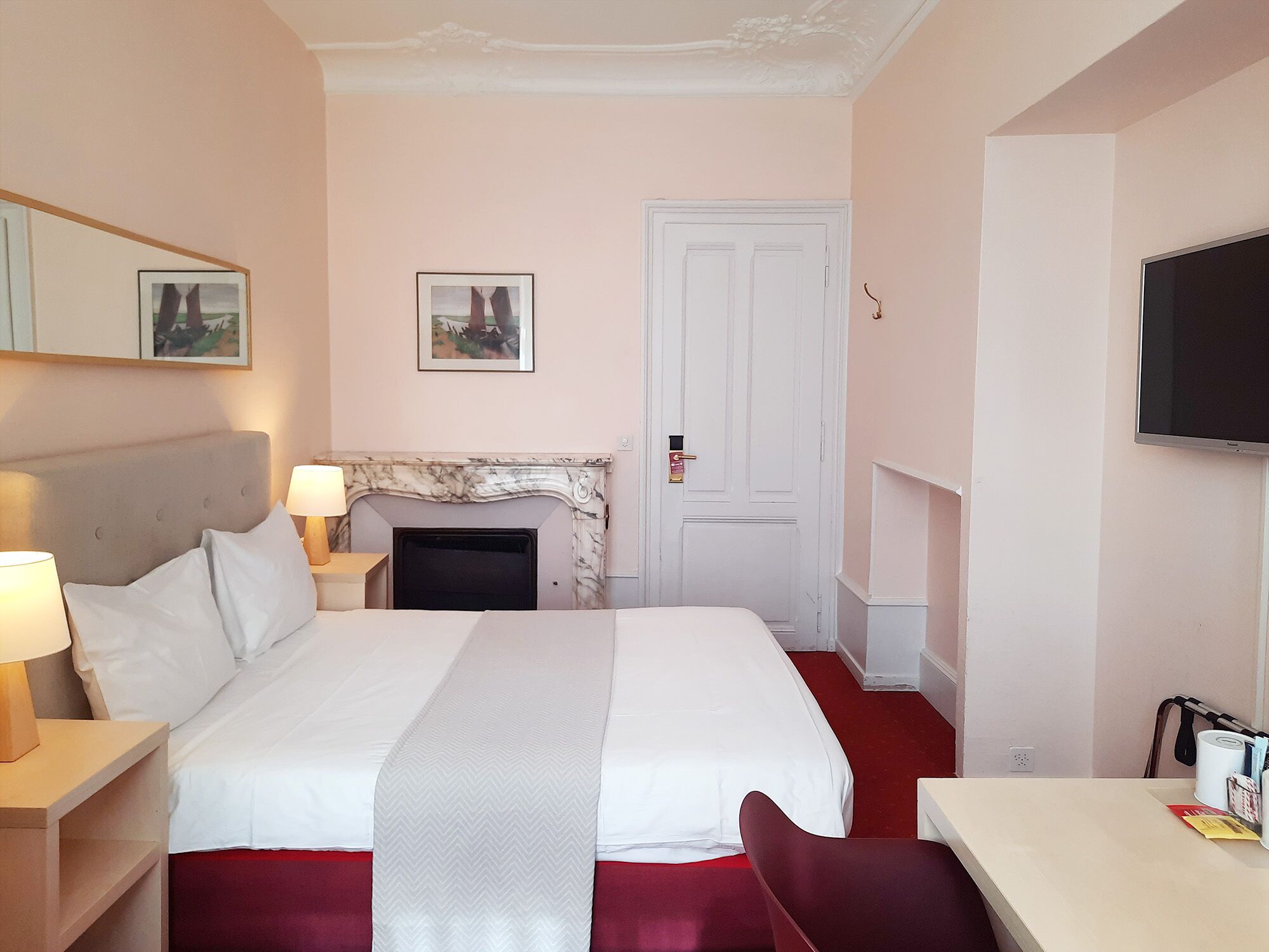 A hotel room with a bed, a fireplace, a television, and a desk.