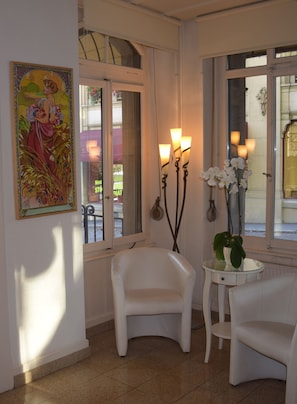 Una habitación con un sillón blanco, una mesa redonda pequeña con una planta en maceta y un cuadro en la pared.