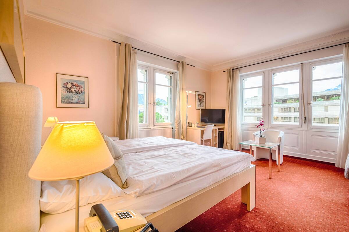 A hotel room with a bed, a desk, a chair, a TV, and a telephone.