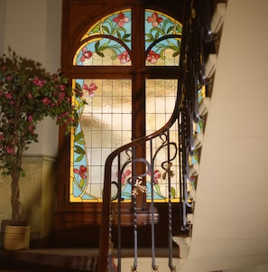 Una escalera con barandilla de hierro forjado que lleva a una puerta con vidrieras decoradas con motivos florales.