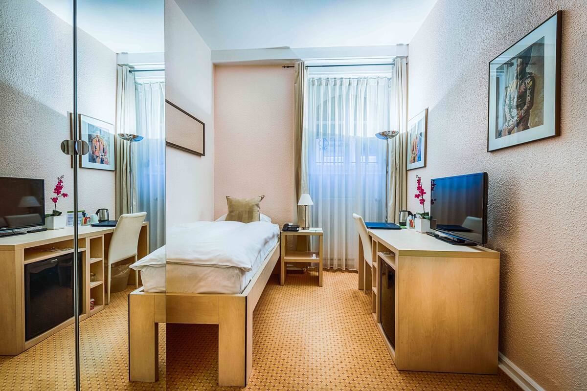 A hotel room with a bed, desk, chair, TV, and a small table.