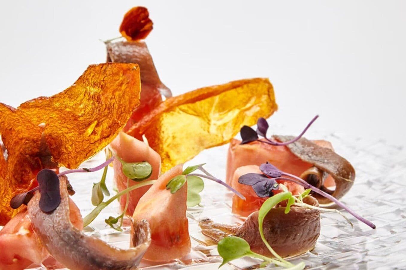 A variety of food items, including what appears to be smoked salmon, pickled vegetables, and possibly some type of cured meat, arranged on a glass surface.
