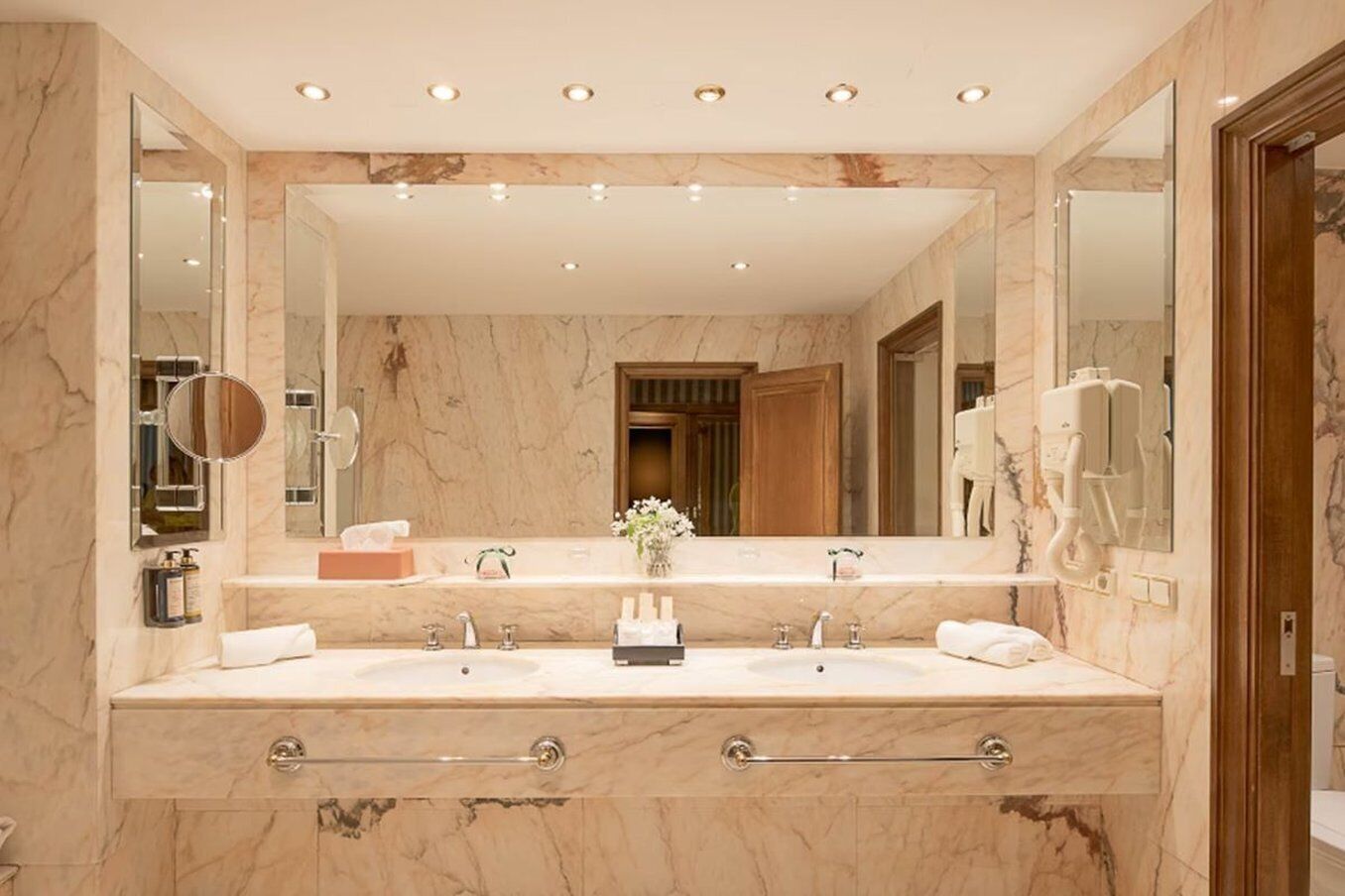 A bathroom with two sinks, marble walls, and a large mirror.