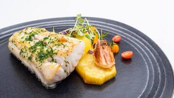Un plato con un trozo de pescado, una rodaja de verdura amarilla y algunas guarniciones.