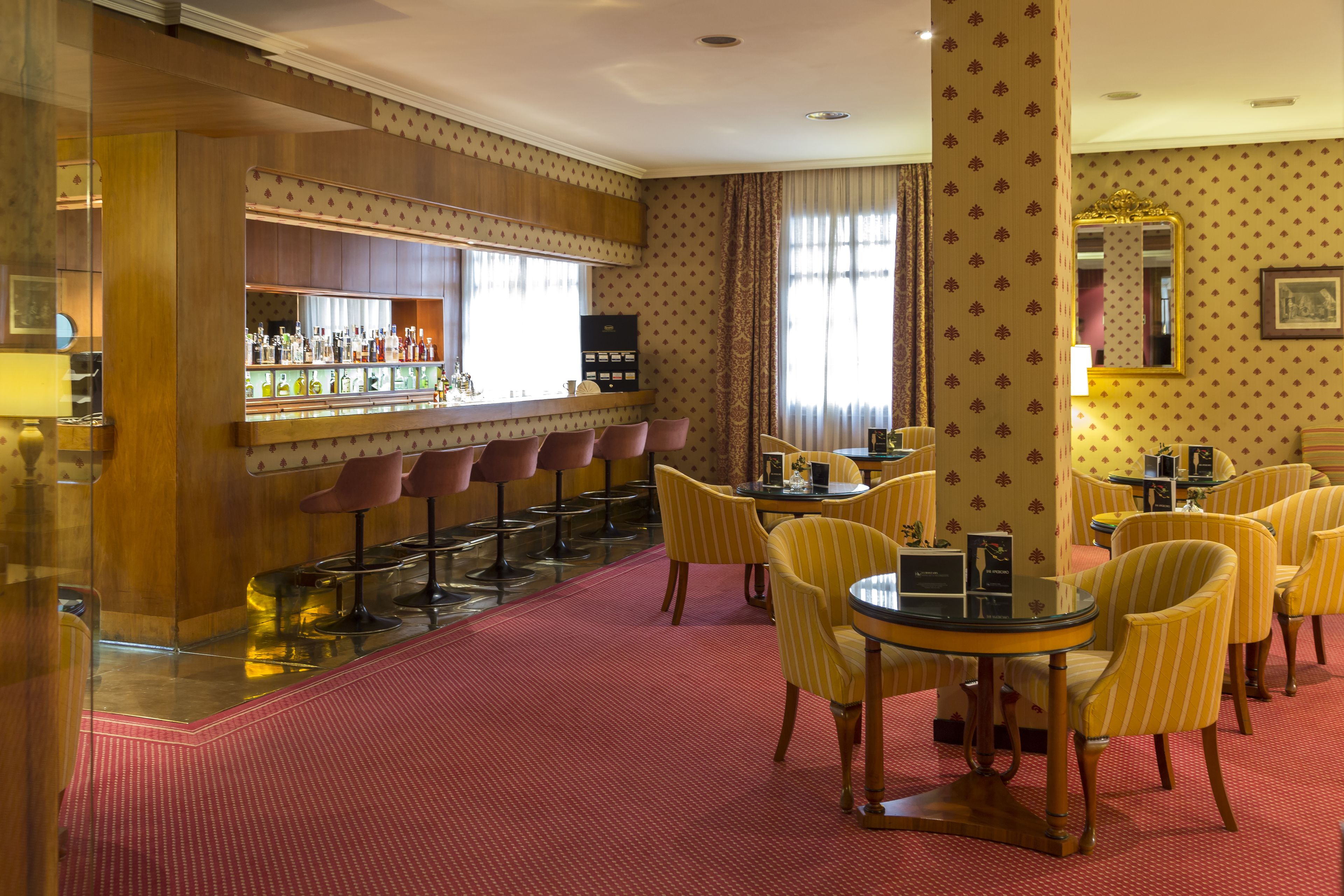 A hotel lobby with a bar area, striped chairs, and a red carpet.