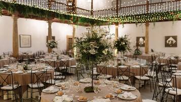 A banquet hall with round tables set for a formal event, featuring floral centerpieces and a warm, inviting atmosphere.
