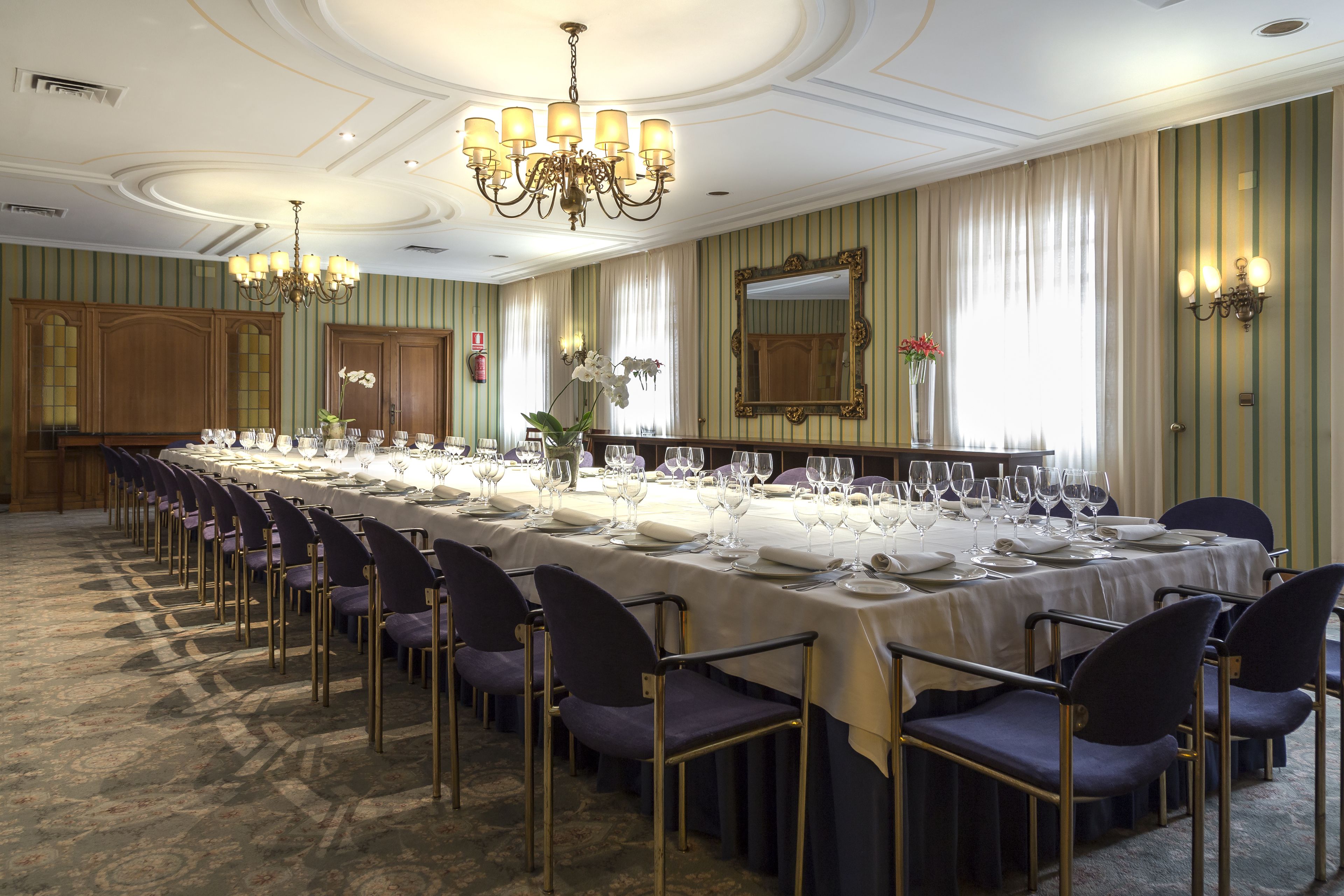 A long banquet table set for a formal event, with chairs on both sides and a chandelier above.