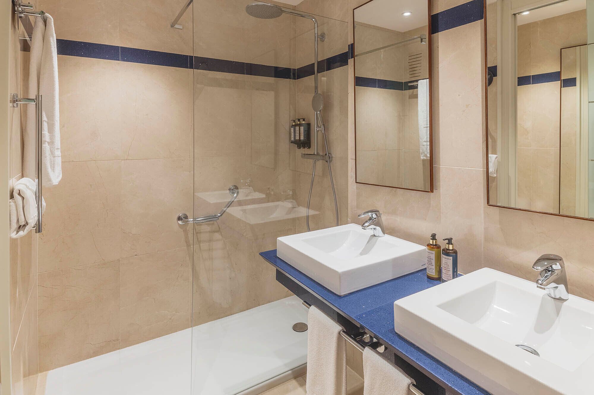 Un baño moderno con dos lavamanos, ducha y zona de ducha con cerramiento de vidrio.