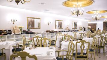 A formal dining room with multiple tables and chairs, elegant chandeliers, and decorative mirrors.