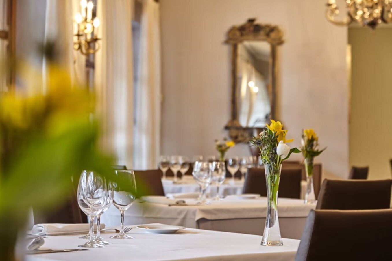 A dining area with tables set for a meal, each with a vase of flowers and wine glasses.