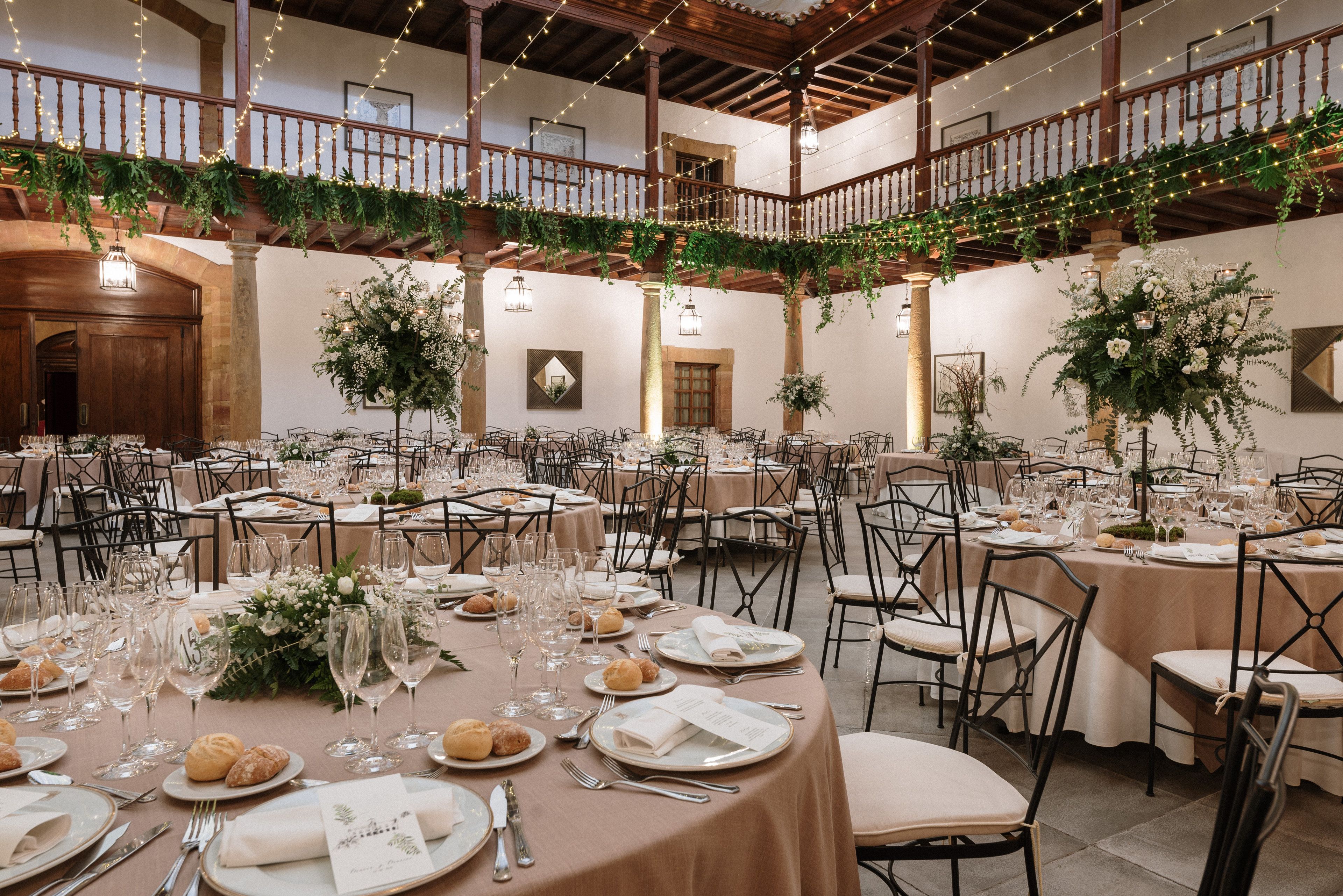 A banquet hall with round tables set for a formal event, featuring floral centerpieces and elegant table settings.
