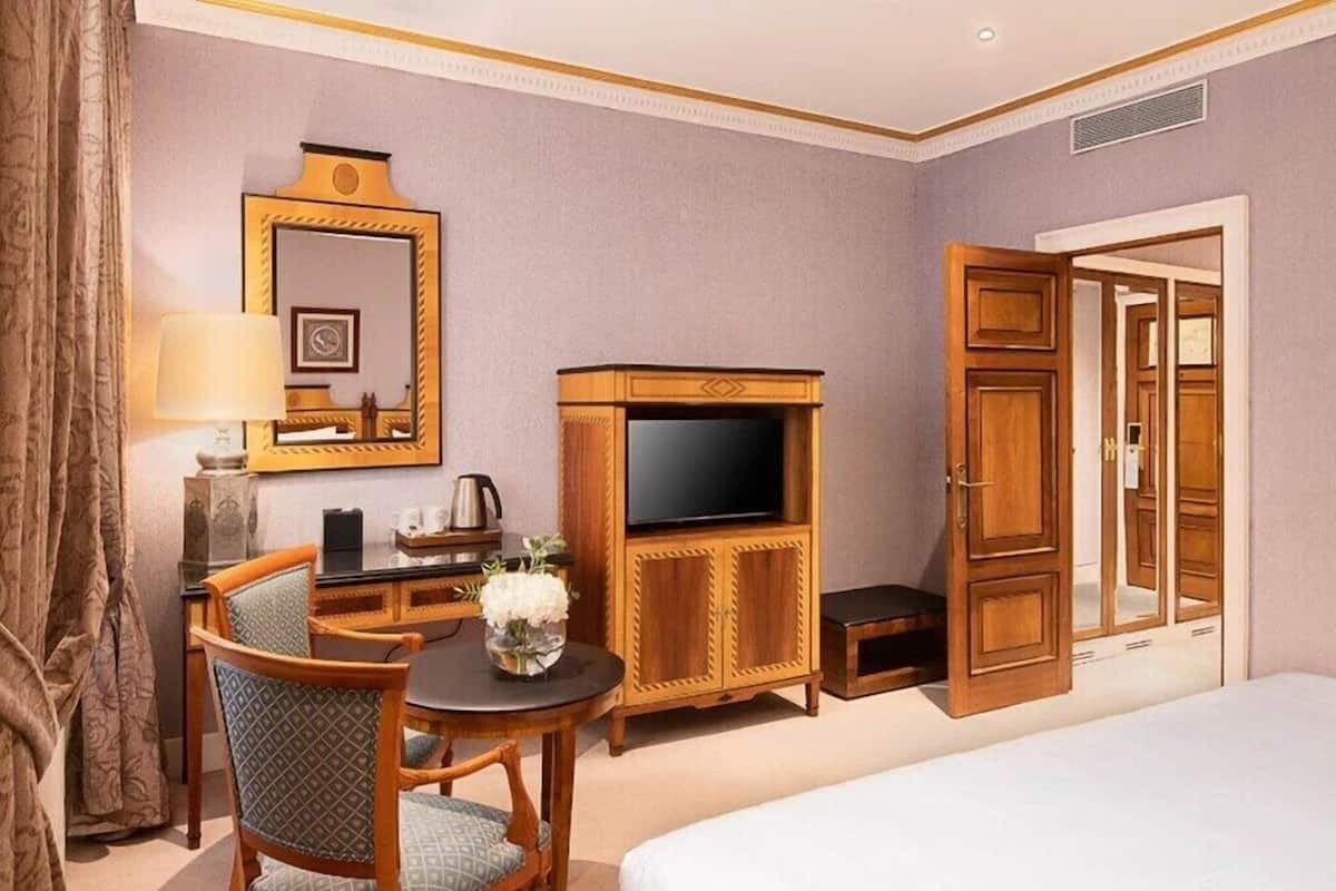 Ein Hotelzimmer mit einem Bett, einem Fernseher, einer Holzkassette, einem Schreibtisch mit Lampe und einem Sessel.